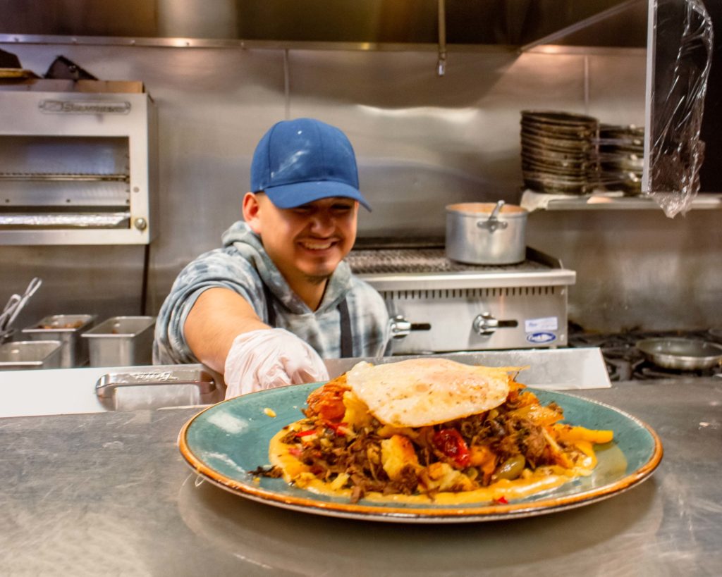 Cook serving a plate of food with a huge smile on his face