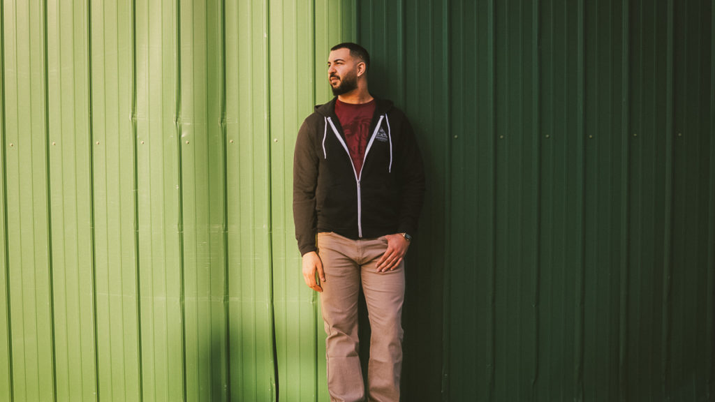 Person standing in front of a green wall wearing a Brewminati zip up hoodie