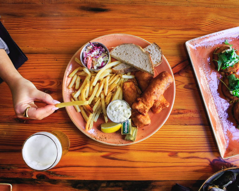 A hand reaching to grab a french fry off of Benelux's Classic Fish Fry plate